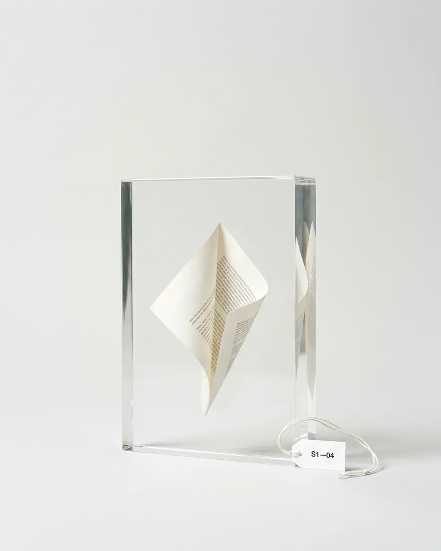 A sheet of paper suspended mid-fold inside a clear acrylic block. The fold tightens.