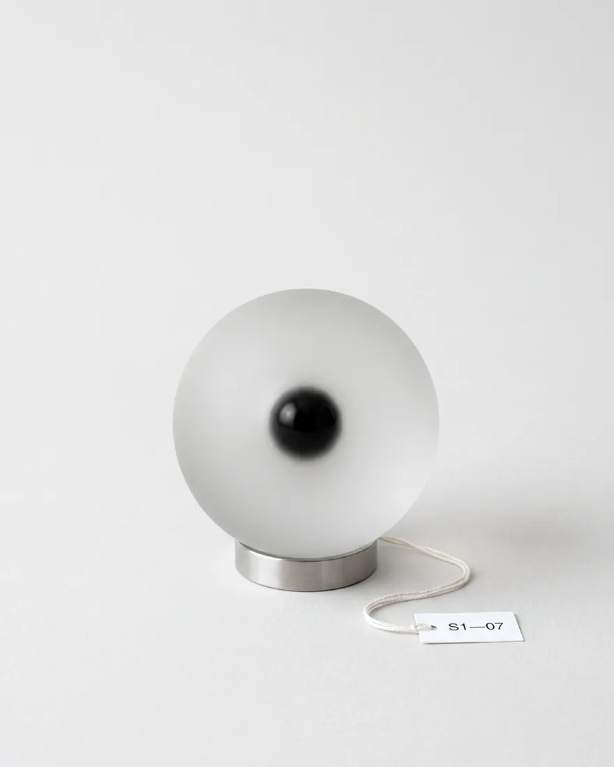 A frosted glass sphere with a black glass core, like an eye, resting on a steel ring.